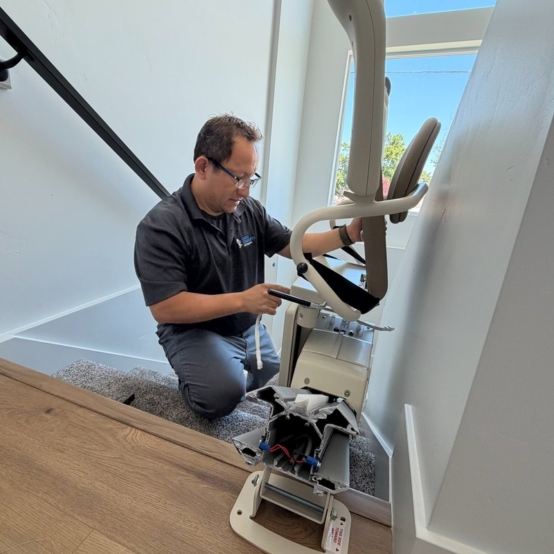 Lazo installer kneeling on a landing, assembling a stair lift seat at the top of the stairs