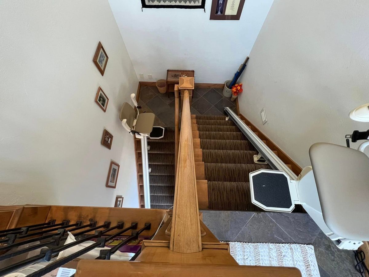 Lazo install: looking down a split stairwell with a stair lift parked at the top of each flight