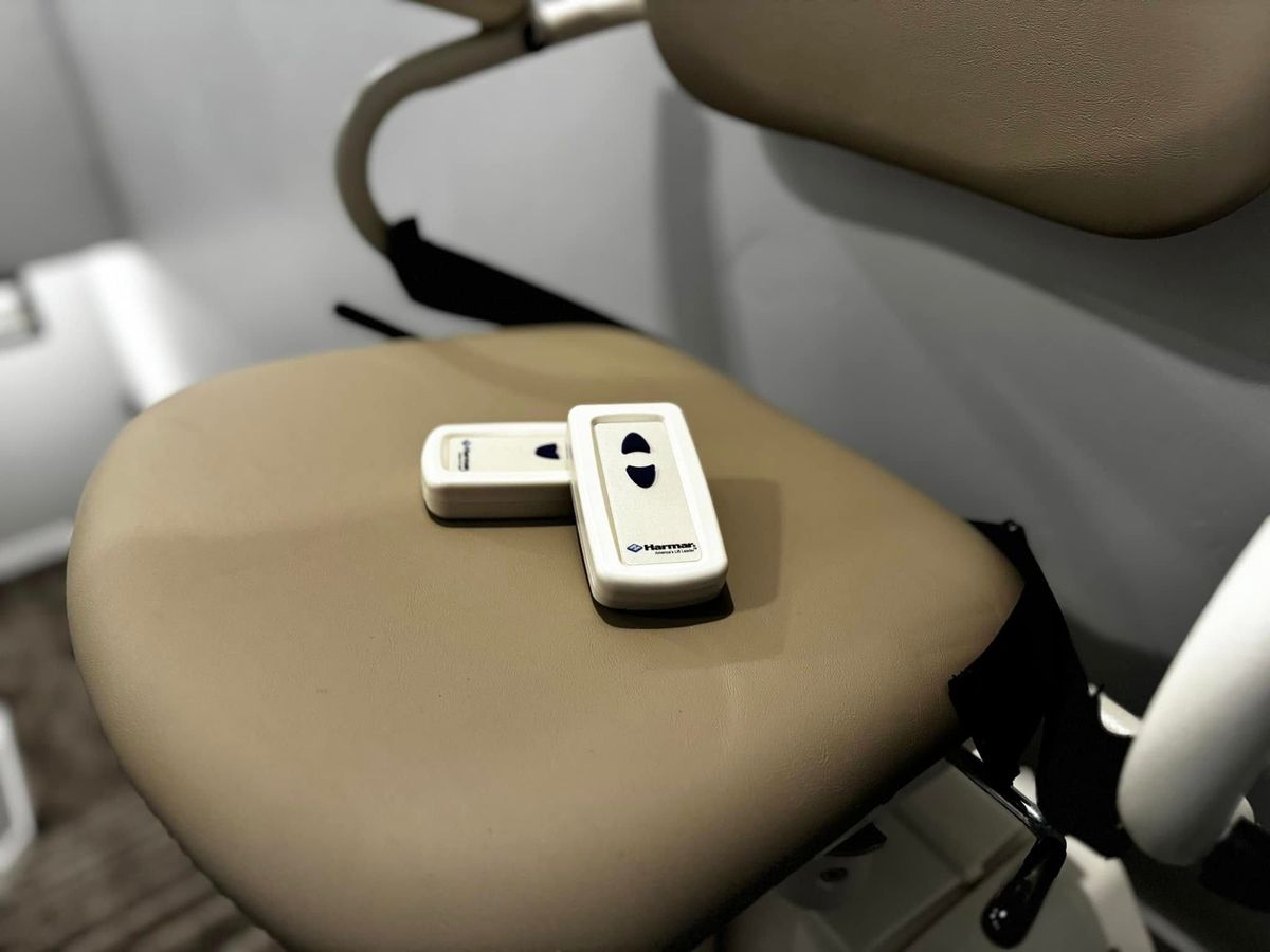 Close-up of two Harmar wireless remotes resting on a tan stair lift seat