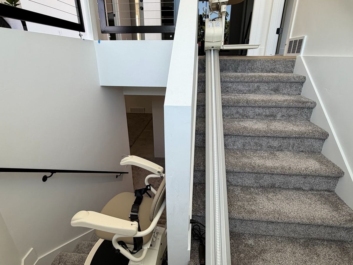 Stair lift rail up a carpeted staircase with the chair parked folded at the lower landing