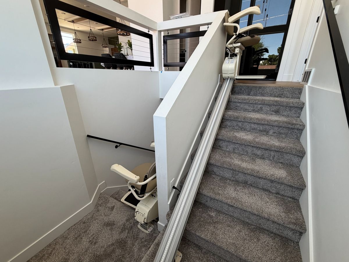 Stair lifts parked at the top and bottom landings of a carpeted staircase