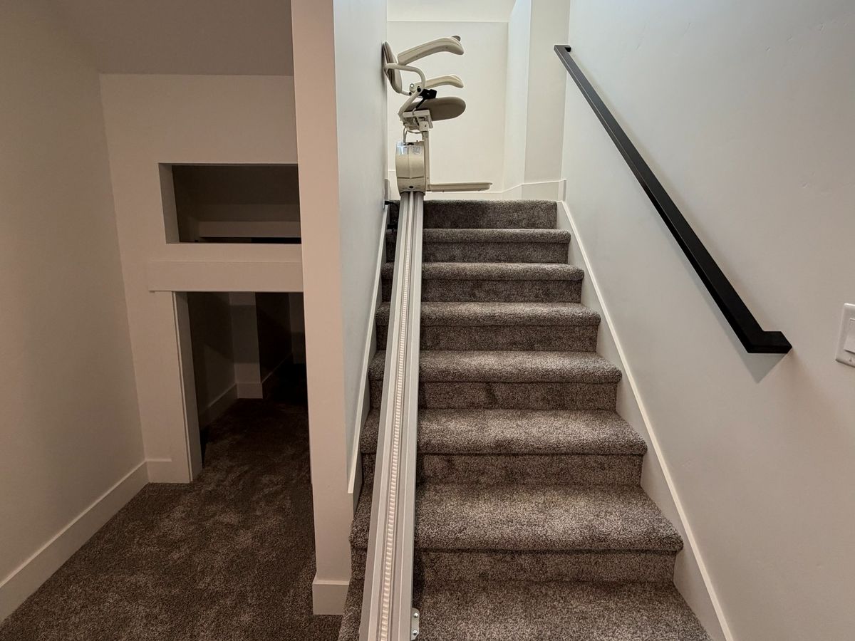 Stair lift rail up a straight carpeted flight, the lift folded at the top under a skylight