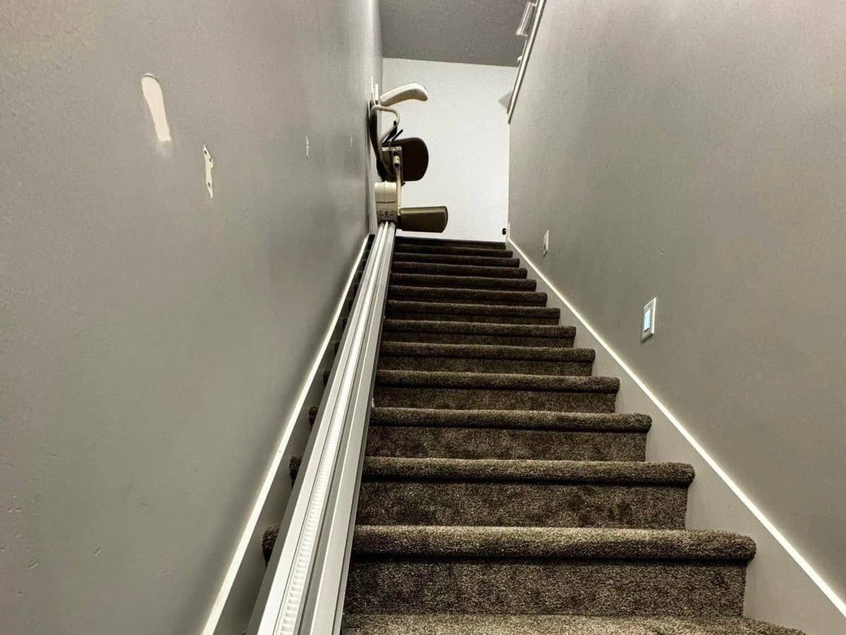Harmar SL300 stair lift rail on a carpeted basement staircase, the lift parked at the top