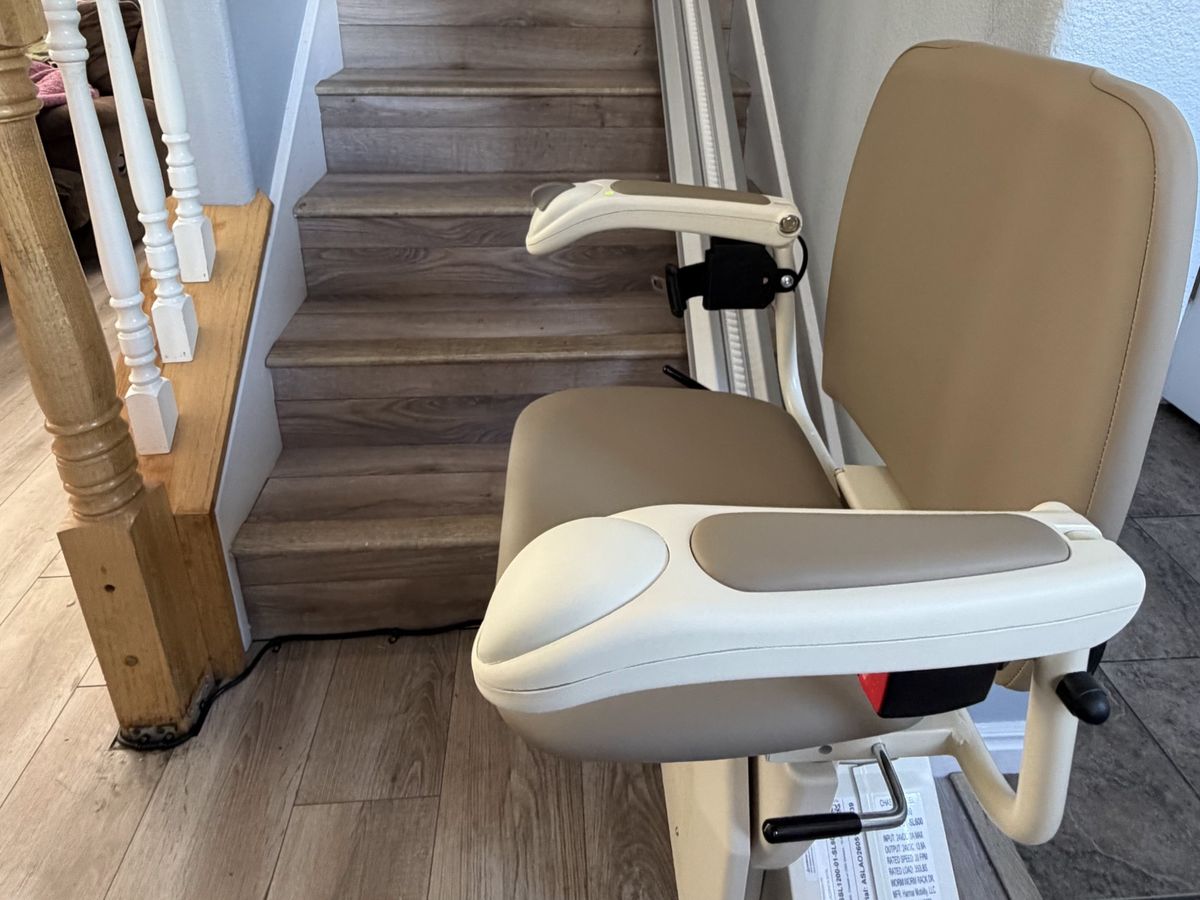 Harmar SL600 stair lift with a tan seat parked at the foot of a staircase with wood-look treads