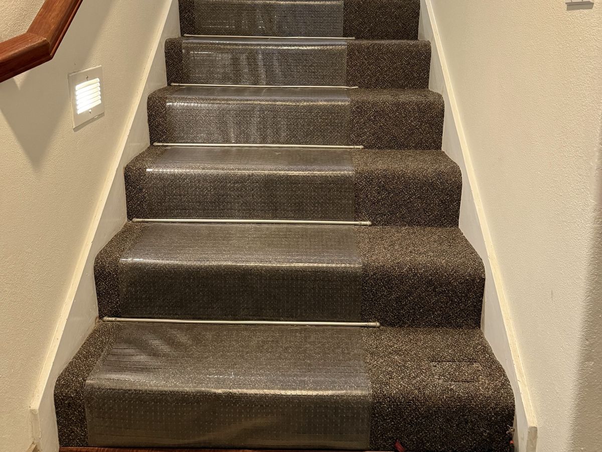 The same carpeted staircase with a wood handrail, before the stair lift was installed