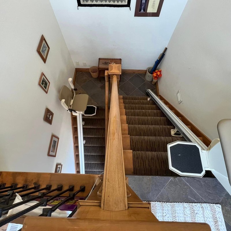 Stair lifts on two flights of a home, seen from the upstairs landing