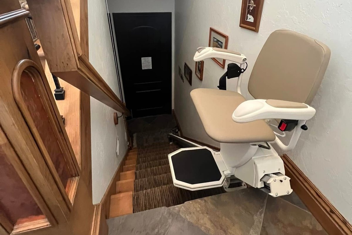 Stair lift with a tan seat parked at the bottom of a short flight in a Utah home