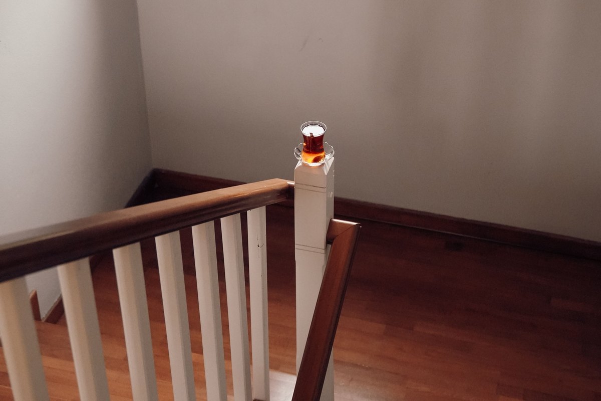 Glass of tea on a white newel post beside a wood handrail at the top of the stairs